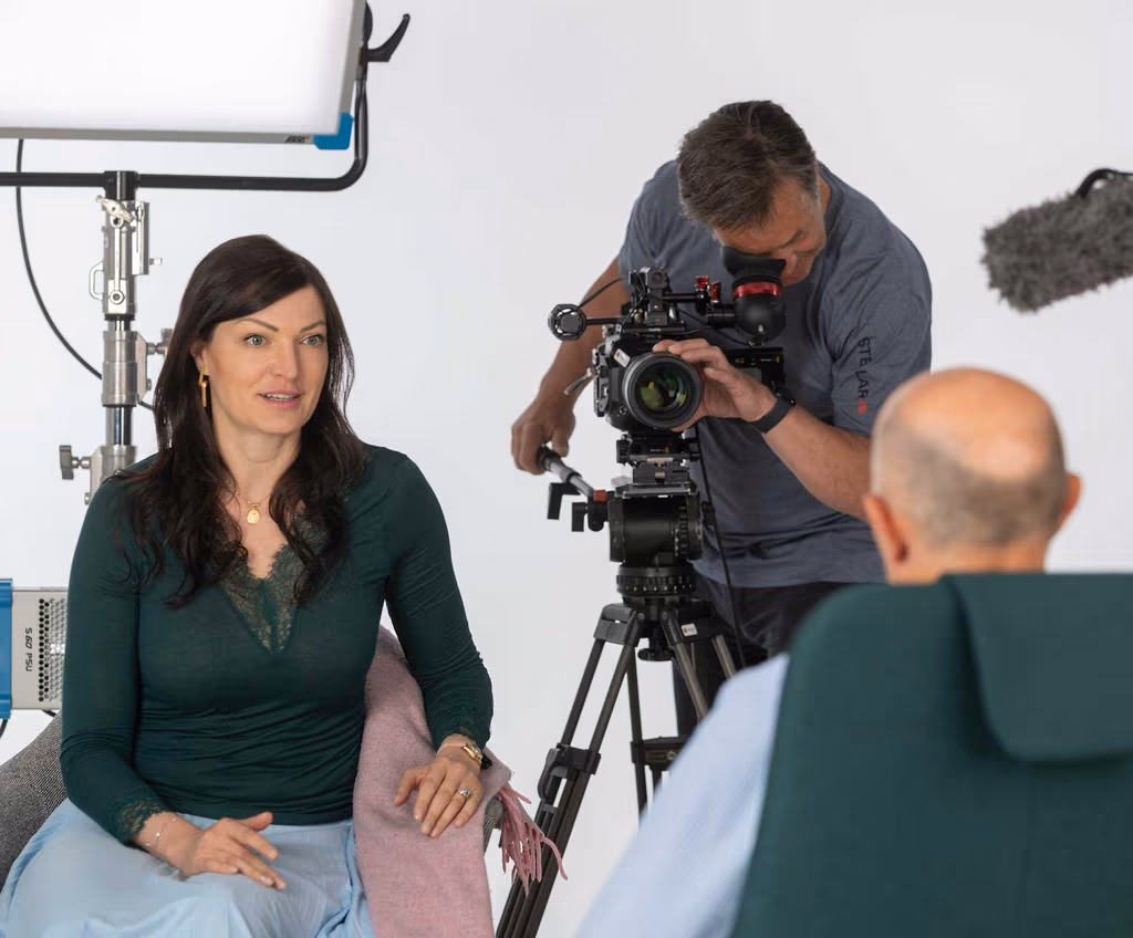 Drei Personen bei einer Interviewaufnahme: eine Frau interviewt
				einen Mann mit Glatze, während ein Kameramann die Szene mit Beleuchtung
				und Mikrofon aufnimmt. 