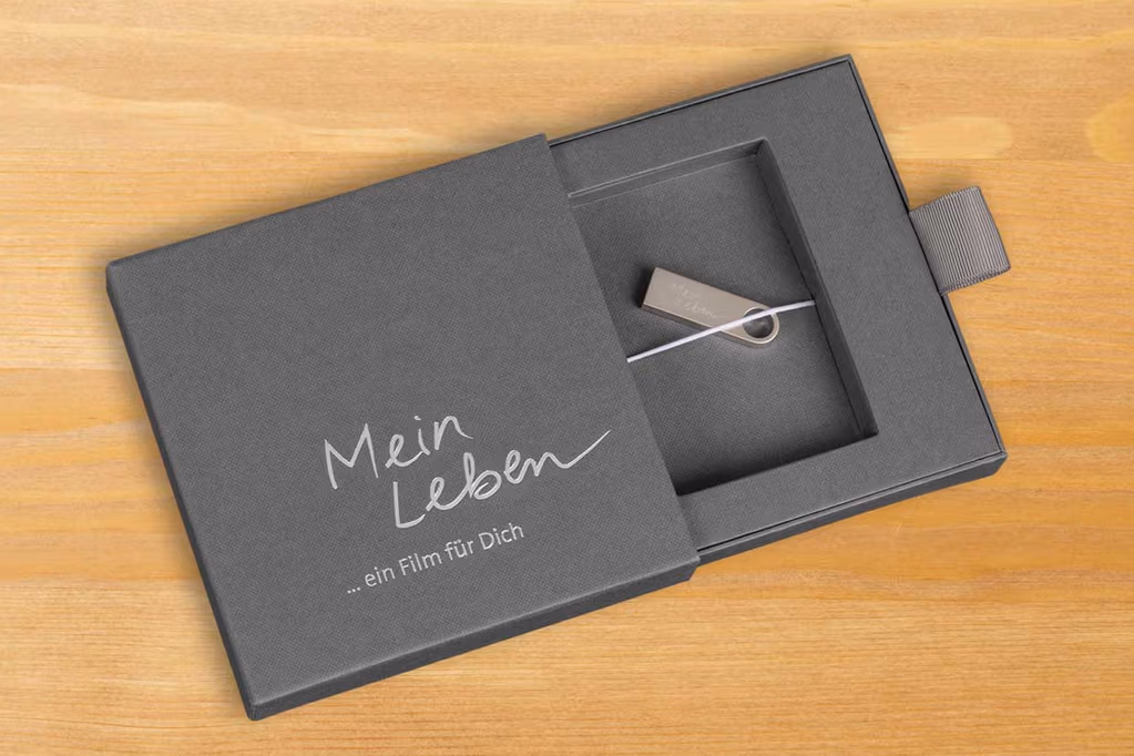 Schwarze Geschenkbox mit der Aufschrift „Mein Leben – ein
				Film für Dich“, geöffnet und mit einem silbernen USB-Stick im Inneren.